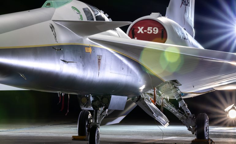 NASA's X-59 airplane sits in its hangar with lights shining on it.