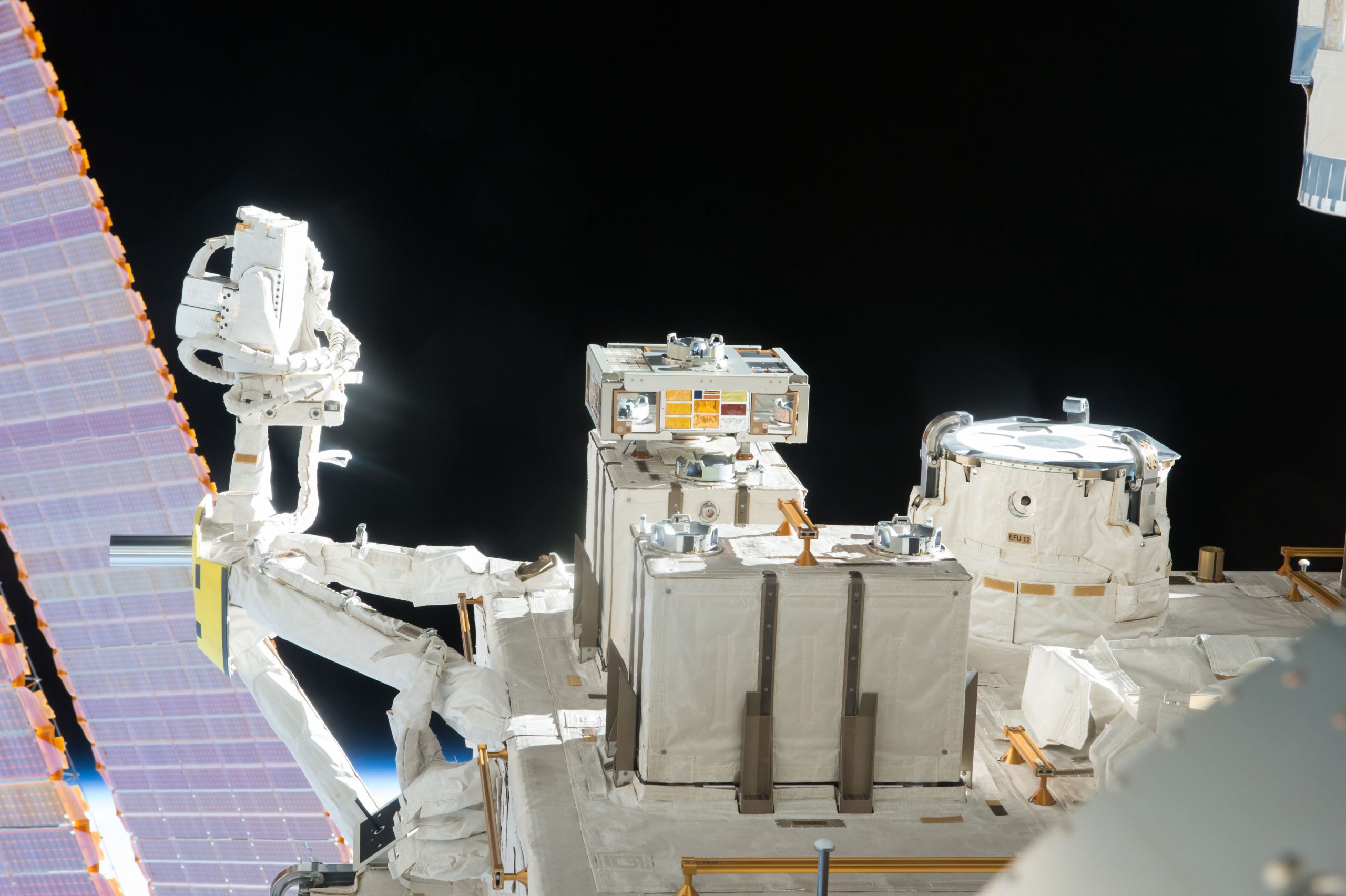 A view of an exposed module outside the International Space Station with solar panels and the darkness of space behind it.