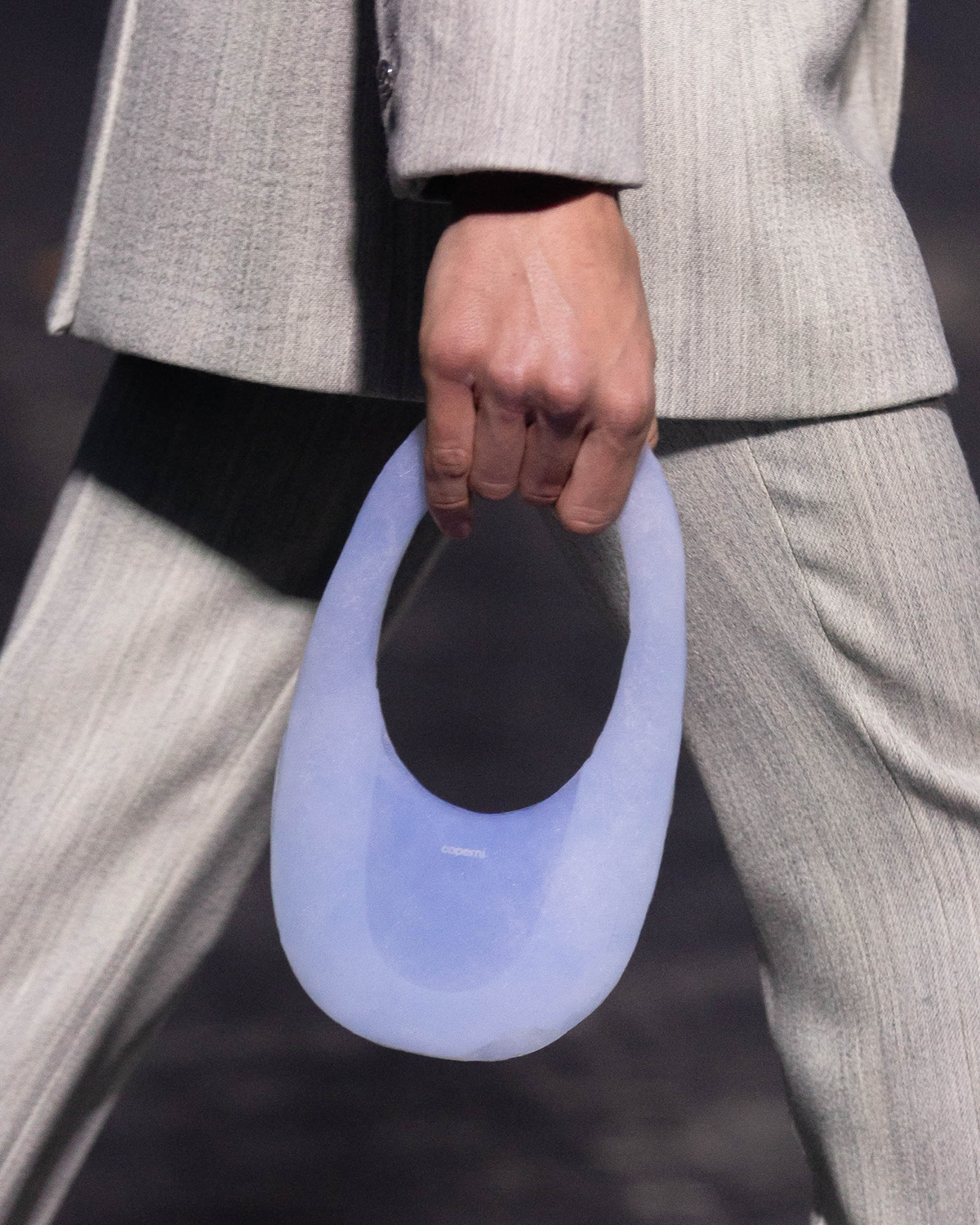 A model holds a small purse made of aerogel, a softly transparent blue color and adorned with the logo of the Coperni fashion brand.