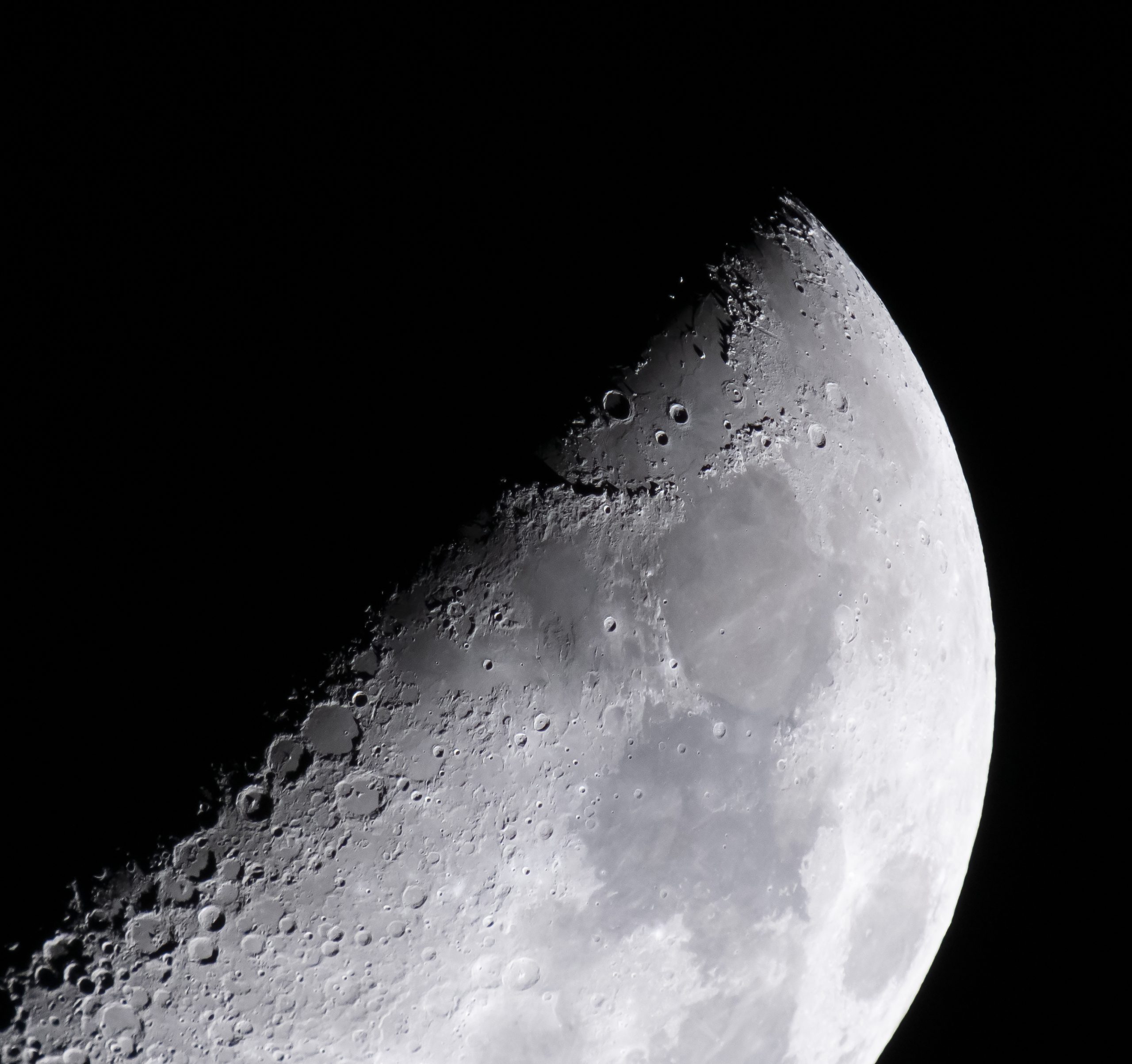 The Moon is lit so only half of it, diagonally, is visible. Along that line, craters of different sizes are visible. As you look toward the right, you can see light and dark gray areas on the Moon's surface. The Apollo 15 landing site