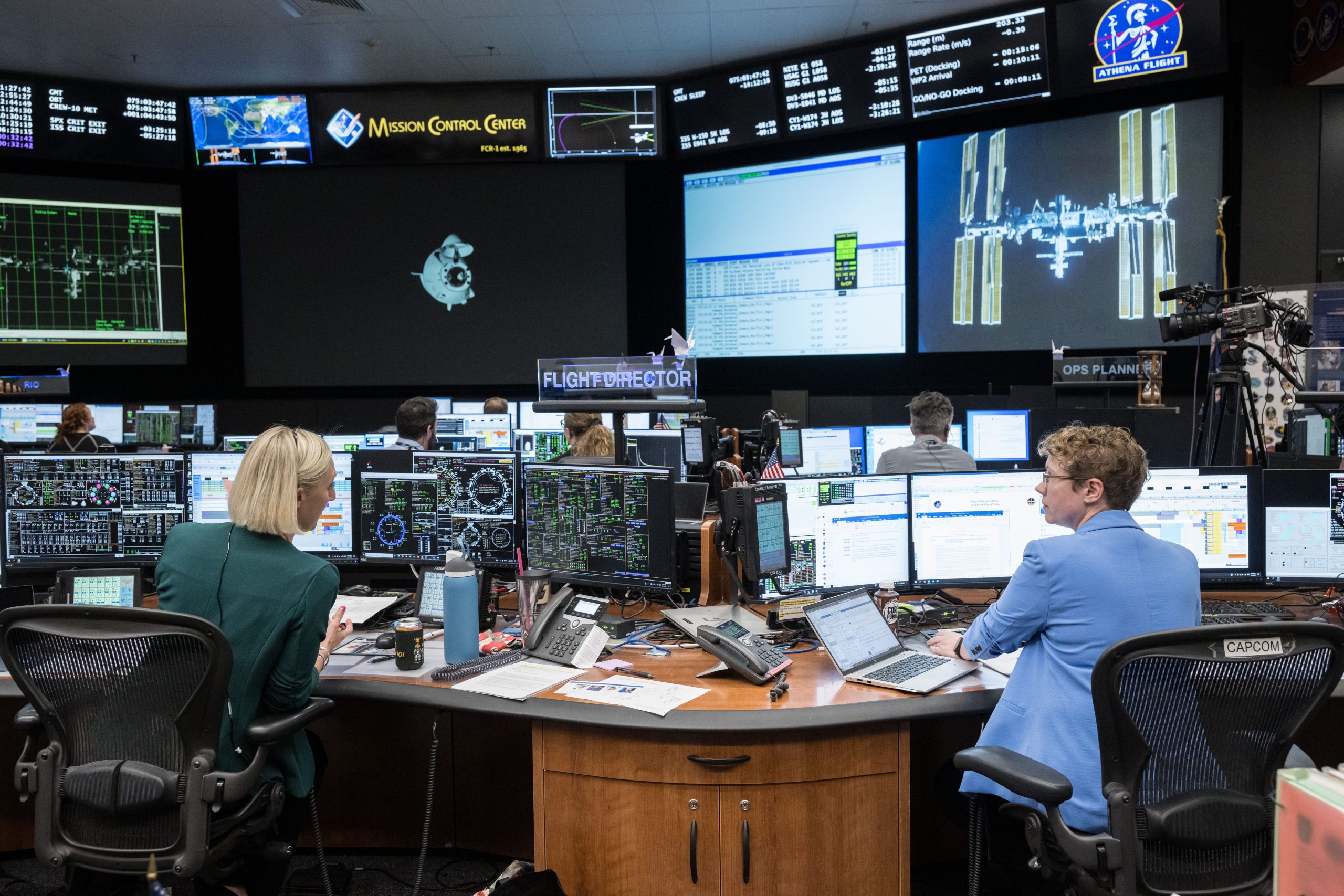 Two women sit at their desk in the Mission Control Center