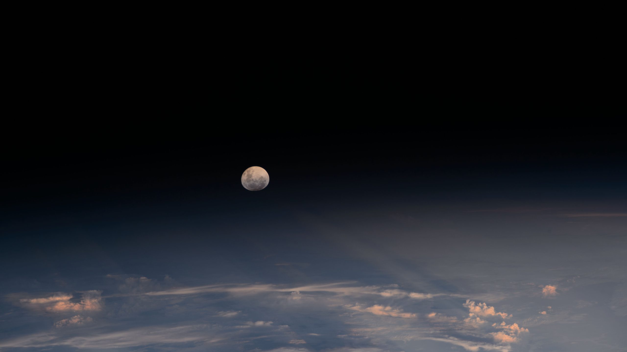 The Moon looks nearly full from the viewpoint of the International Space Station. Below, we can see the Moon's light being refracted by Earth's atmosphere. A few clouds can be seen at the bottom of the image.