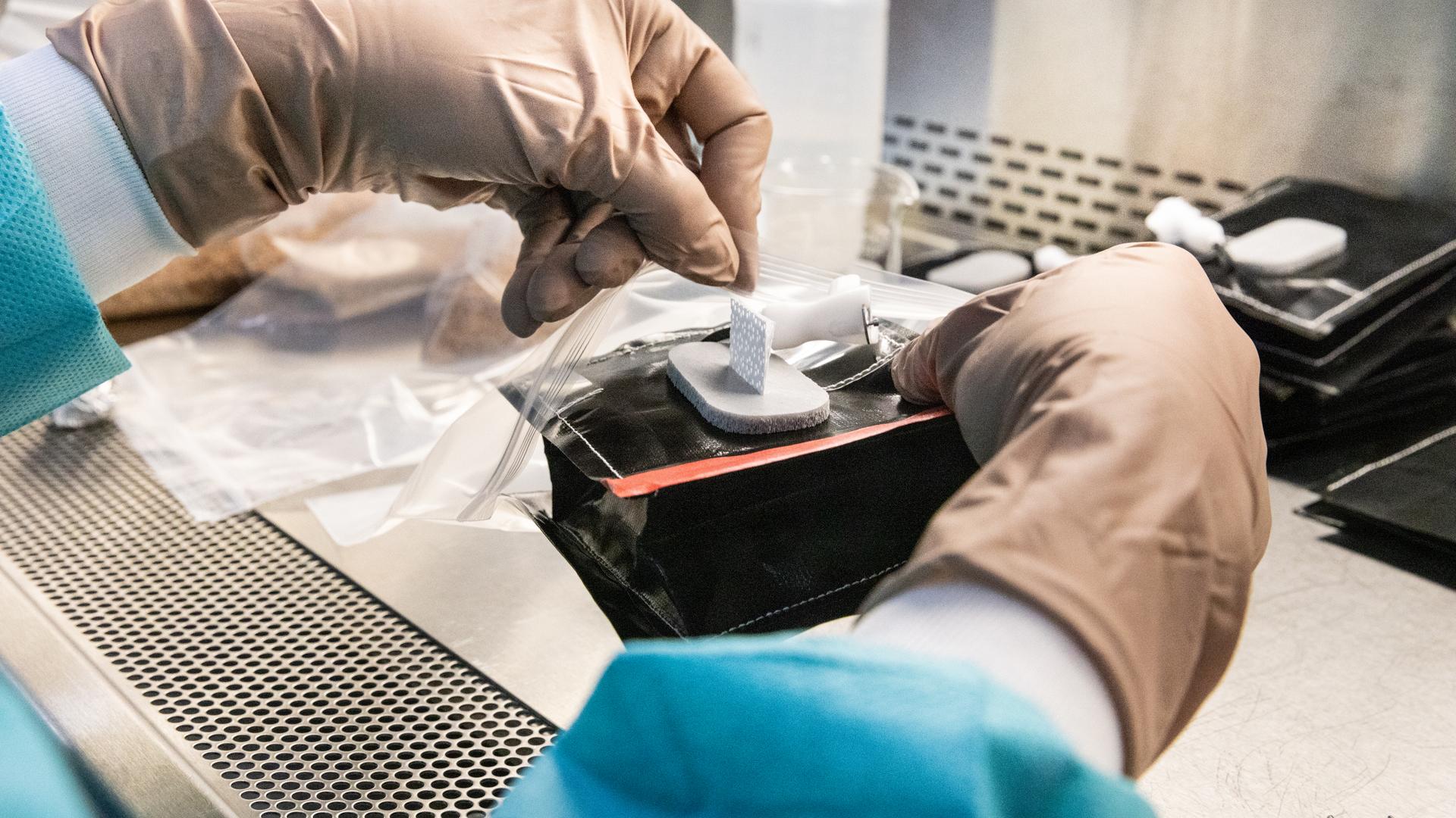 A researcher in protective clothing and gloves works at a laboratory station, preparing components for plant growth experiments.
