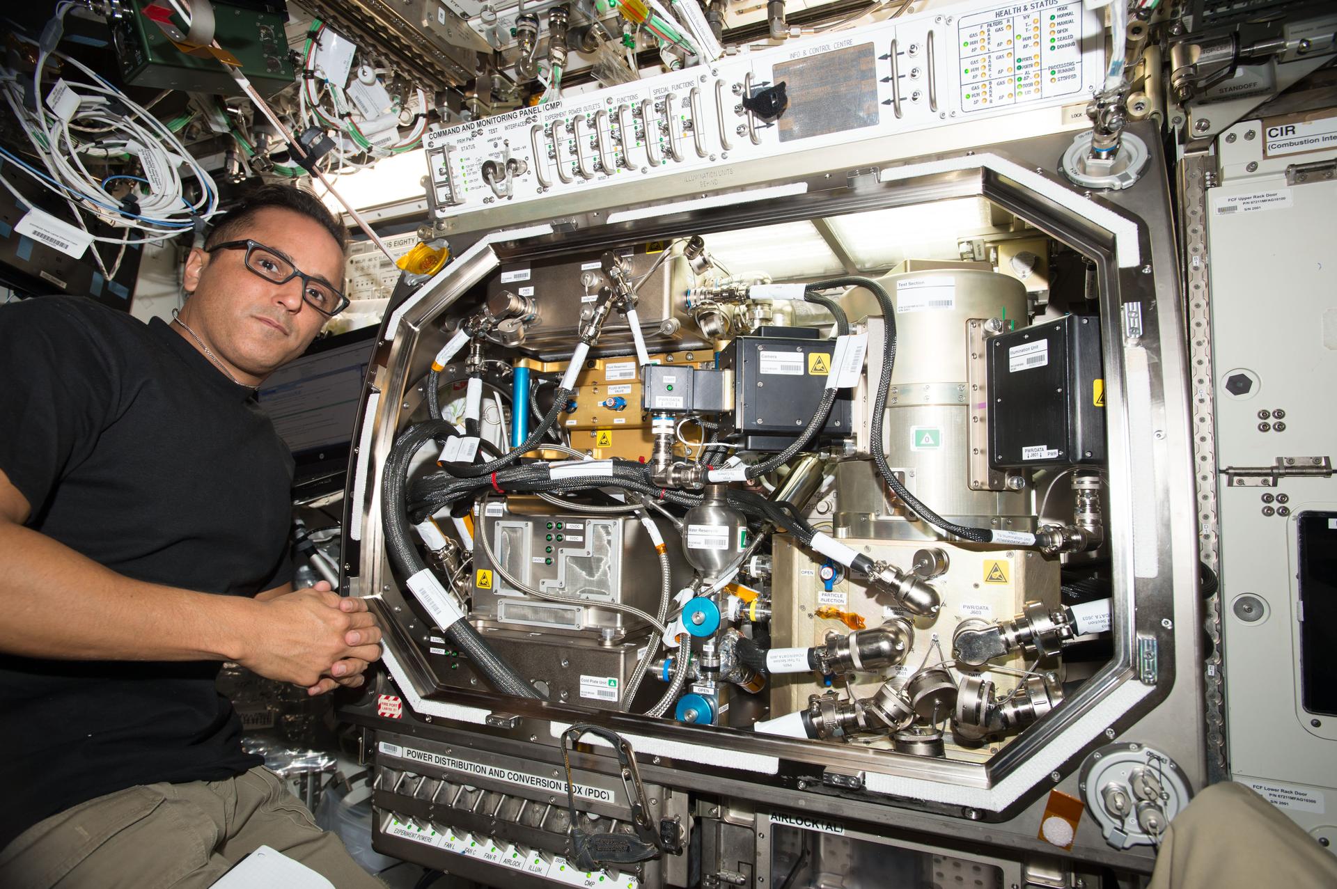 Astronaut in glasses working with scientific equipment inside an International Space Station laboratory.