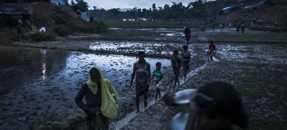 Rohingya refugees walk across a muddy field in southern Bangladesh, as fires burn in a distance. (file photograph) Rohingya refugees walk across a muddy field in southern Bangladesh, as fires burn in a distance. (file photograph)