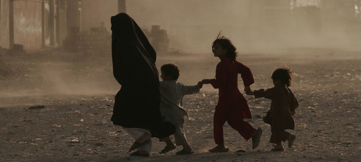A family runs across a dusty street in Herat, Afghanistan.