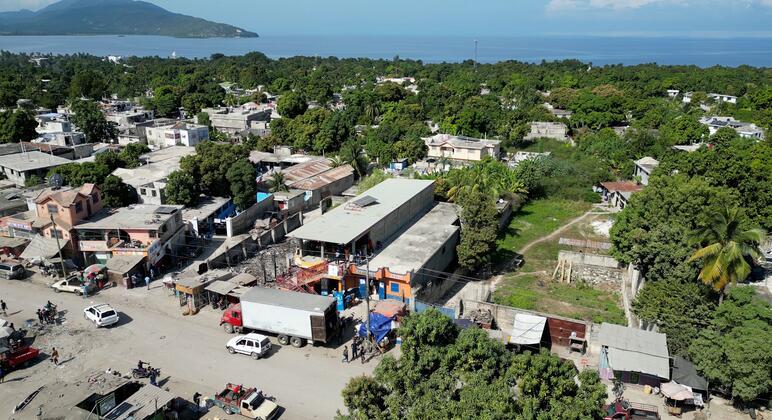 An aerial view of a Haitian community affected by a storm, showing houses, roads, and vehicles, with WFP providing food assistance through a voucher system.