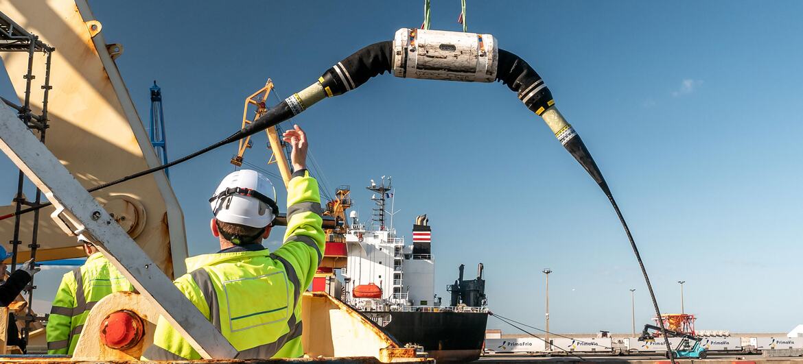 A worker in a high-visibility vest and hard hat directs the deployment of a large submarine cable from a ship at a port in Porto, Portugal, during the International Submarine Cable Resilience Summit 2026.