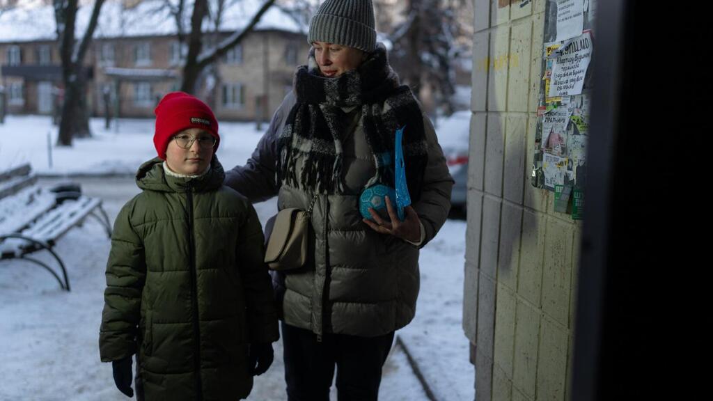 A woman and a child dressed in winter clothing stand outside a building in a snowy urban setting in Ukraine.
