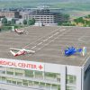 An artist’s concept image shows the square, gray rooftop of a hospital building with three concept aircraft sitting on top. One aircraft is painted dark blue, and two are painted with red and white paint schemes. Each aircraft has several unique propellors and wings to showcase that these aircraft can take off and land on short runways or vertically. The words “Century Medical Center” – in red – sit below the rooftop landing pad with several rows of windows underneath. In the background, there are several rows of trees, buildings, and parking garages, to show that this building is inside of a city.