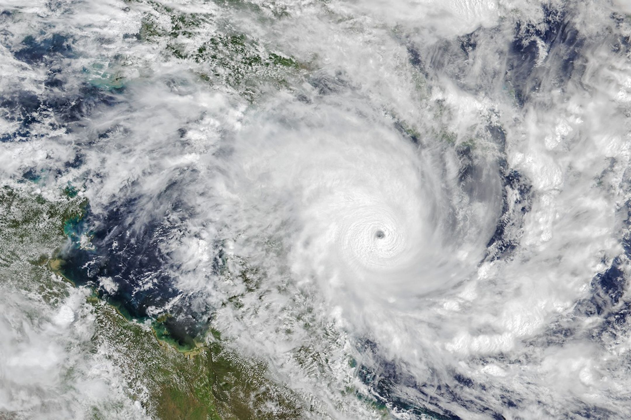 A tropical cyclone with spiraling clouds and a well-defined eye sits off the coast of Queensland, Australia.