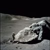 Harrison Schmitt stands next to a giant boulder on the Moon in this photo taken from a distance.