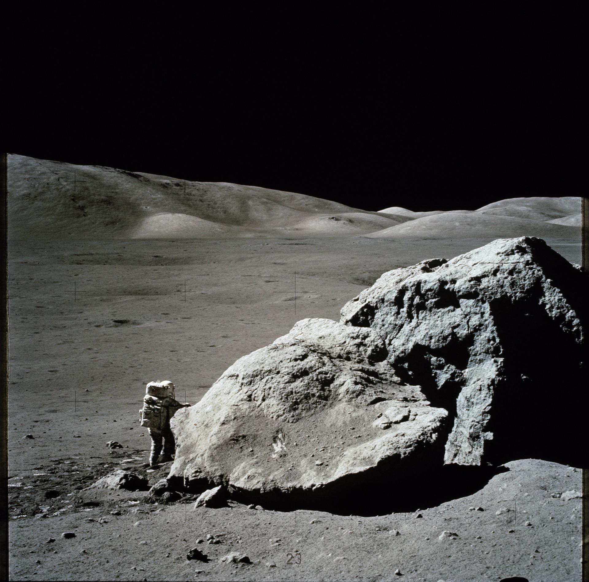 Harrison Schmitt stands next to a giant boulder on the Moon in this photo taken from a distance.