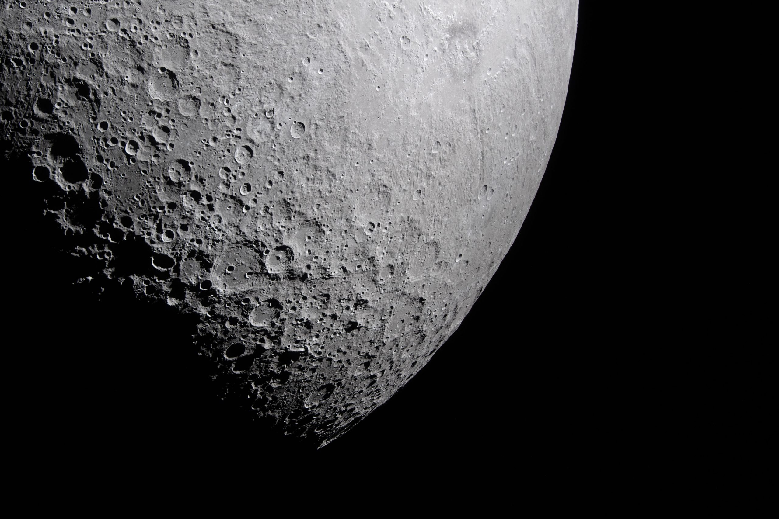 Part of the Moon stands out against the blackness of space. Its surface is marked with many craters of different sizes. The craters are mostly on the left and bottom. The upper right portion of the Moon's surface is much smoother.